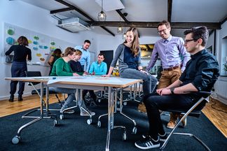 e-pixler-Mitarbeiter bei einer Team-Besprechung in einem modernen Büro mit Whiteboards und Schreibtischen.