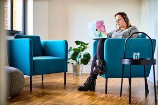 e-pixler-Mitarbeiterin arbeitet mit Kopfhörern und Laptop in einem Lounge-Bereich mit blauen Sesseln und Pflanzen.