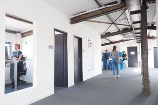 Büroflur bei e-pixler mit Mitarbeitern, die an ihren Arbeitsplätzen sitzen oder sich unterhalten.