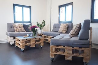 Moderner Lounge-Bereich mit Palettenmöbeln, grauen Polstern und dekorativen Pflanzen.