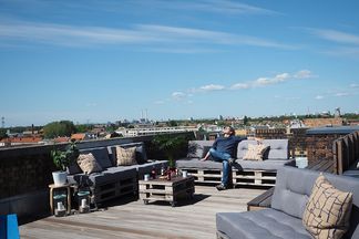 Dachterrasse bei e-pixler mit Palettenmöbeln, Kissen und einem weiten Blick über die Stadt.