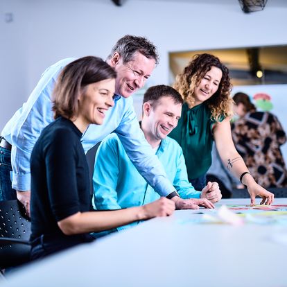 Mitarbeiter bei e-pixler arbeiten zusammen an einem Tisch und diskutieren Ideen auf der Karriereseite.