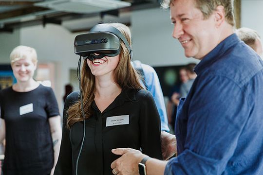 Mitarbeiterin bei e-pixler trägt eine VR-Brille während eines Events, begleitet von einem weiteren Mitarbeiter.